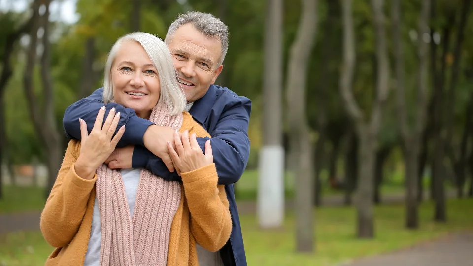An older man hugging his wife from behind in a park